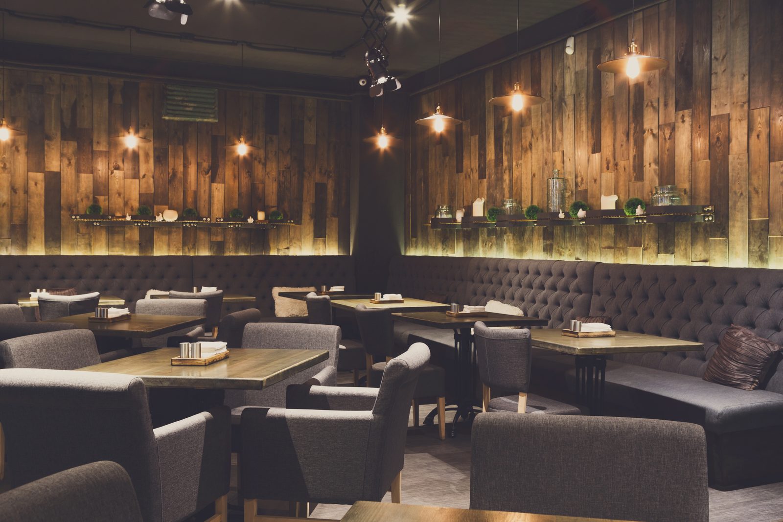 Salle de restaurant dressée, tables et banquettes sous les suspensions